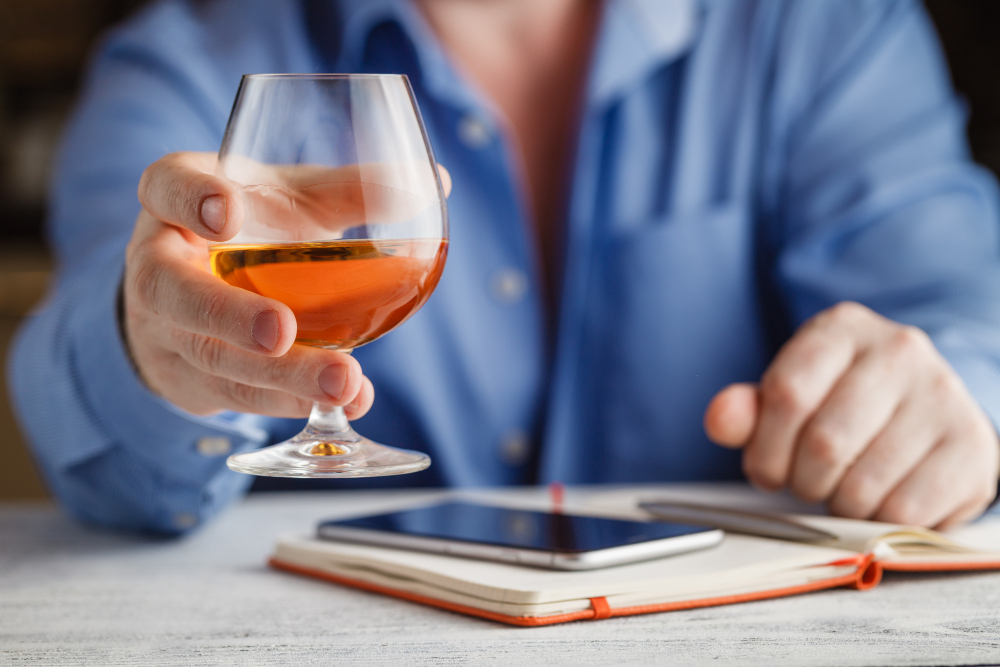 Persoană ținând un pahar cu alcool lângă telefon
