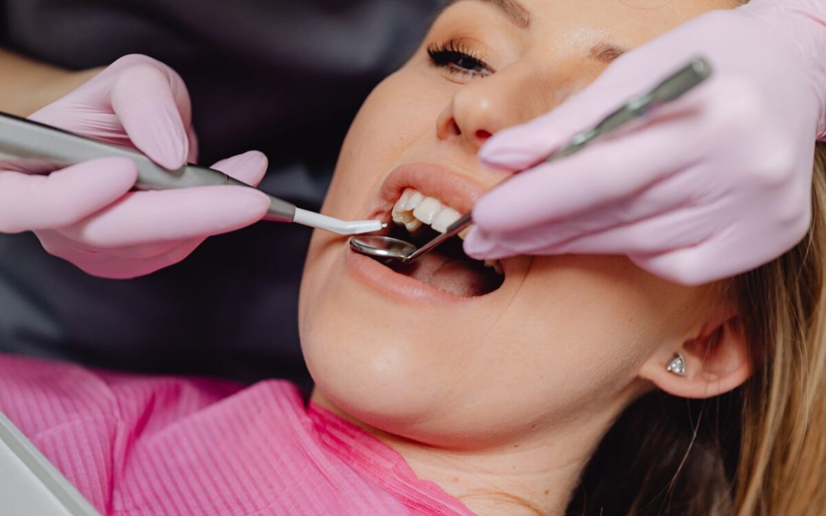 Femeie la consultație stomatologică cu instrumente dentare în gură